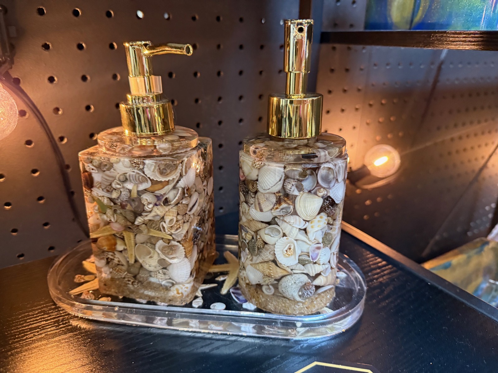 Pair of clear resin soap dispensers filled with seashells and sand, gold pumps on a matching tray
