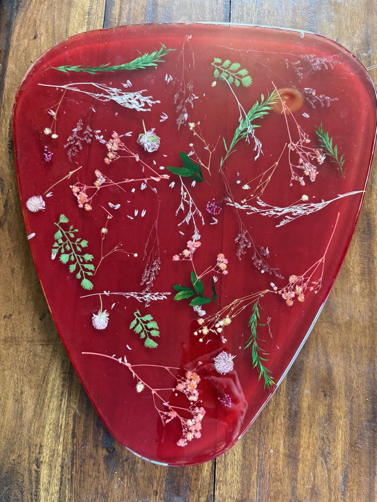 Shield-shaped deep red resin board with pressed herbs, greenery, and dried blossoms