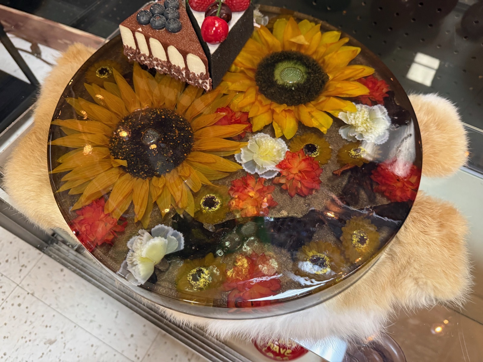 Round resin serving board with sunflowers and colorful flowers under glass-like resin, topped with desserts
