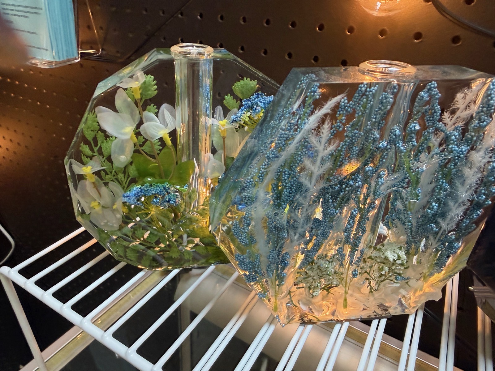 Two geometric clear resin vases with white orchids and blue dried florals embedded inside